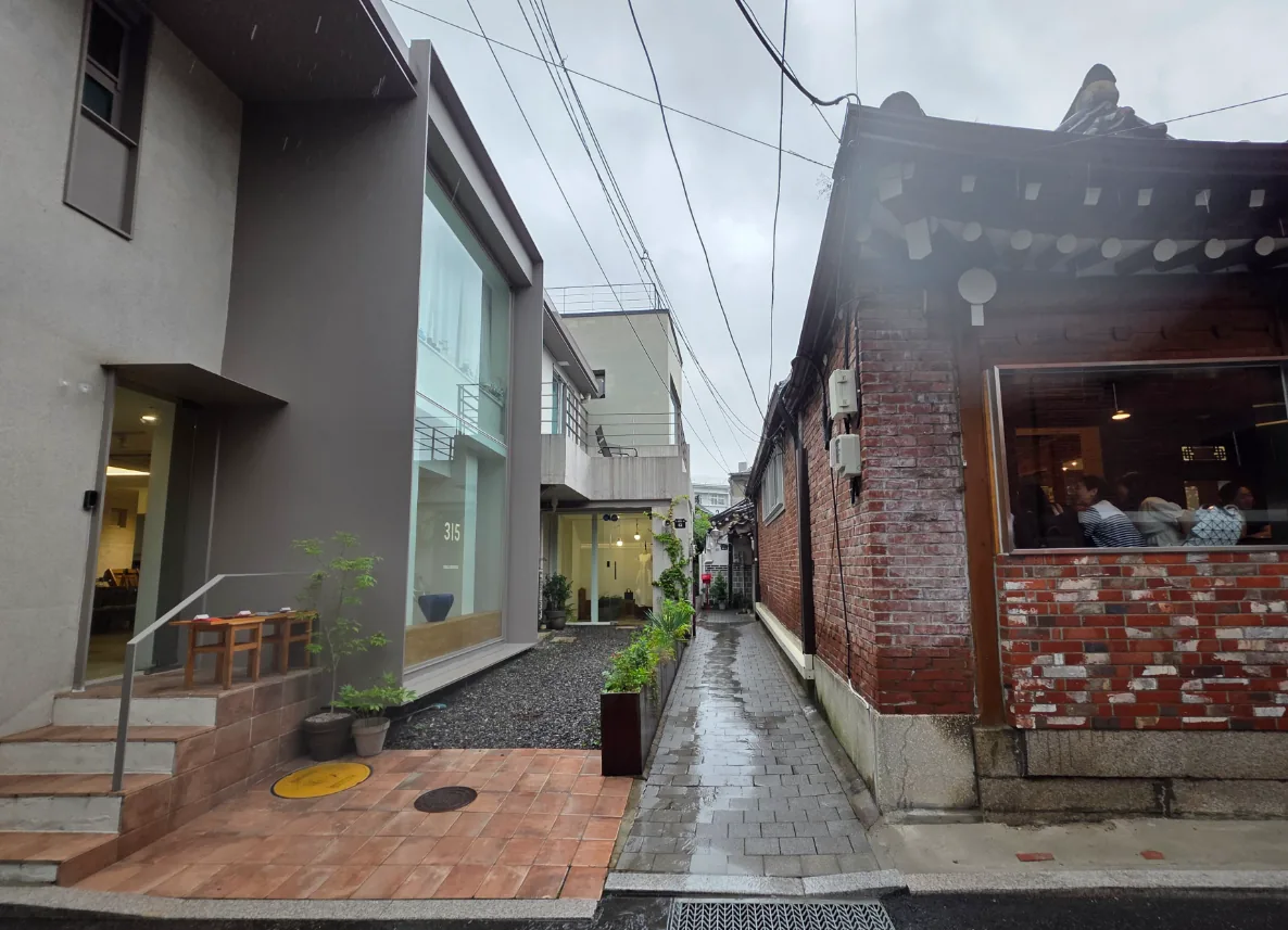 사간동 12-3 앞 북촌 골목 – 붉은 벽돌 한옥 측면과 현대식 건물이 마주한 좁은 길