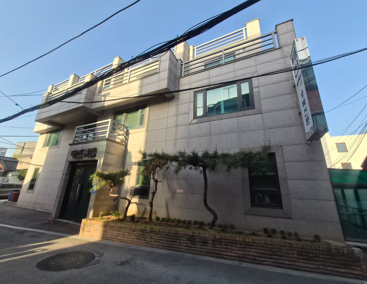 통의동 92 외관 – 소나무 조경을 두른 화강석 마감과 옥상 난간이 보이는 측면